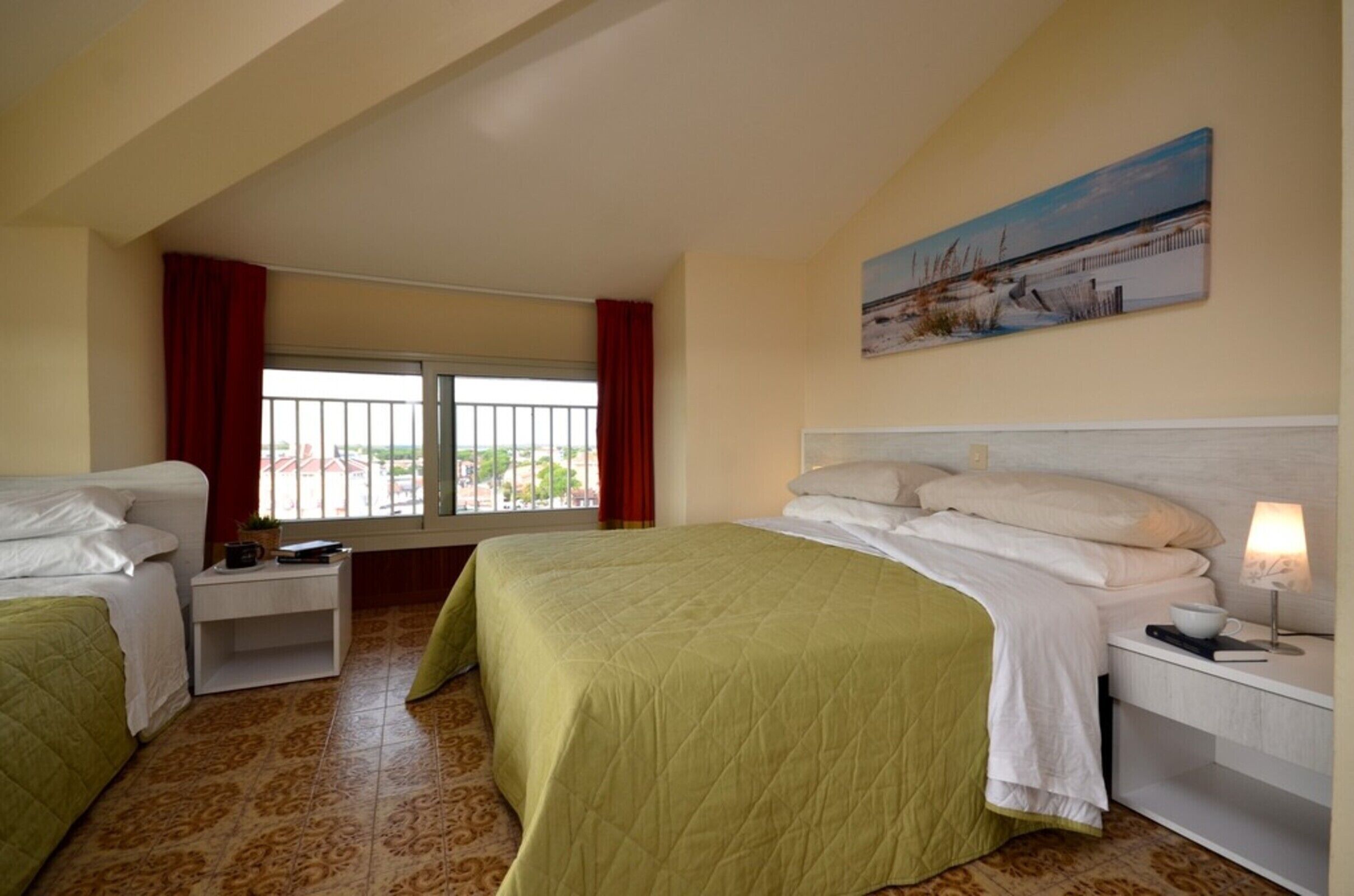 A hotel room with two beds, a window with a view, a painting on the wall, and a nightstand with a lamp.