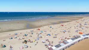 A beach with numerous sunbeds and umbrellas, a sandy shore, and a clear blue sky.