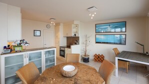 A modern kitchen with a dining area, featuring a granite countertop, white cabinets, and a dining table with wicker chairs.