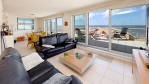 A spacious living room with a large black leather sofa, a coffee table, and a view of the ocean through large windows.