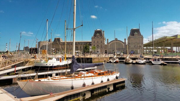 A marina with boats docked, a large building with a clock tower, and a covered area with seating.