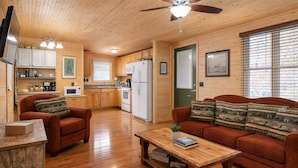 Ein gemütliches Interieur im Chalet-Stil mit Holzböden, einem Essbereich, einer Küche mit modernen Geräten und einem Wohnzimmer mit Sofa und Couchtisch.