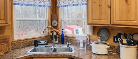 A kitchen with wooden cabinets, granite countertops, a double sink, a coffee maker, and a dish rack.