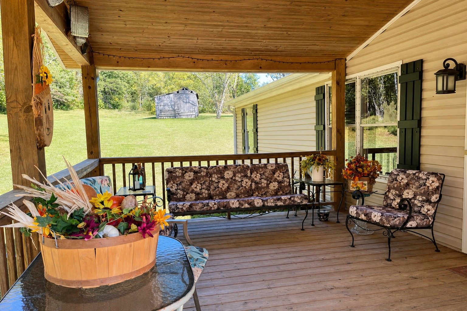 A covered porch with a wooden bench, a table with a vase of flowers, and a view of a house and yard.