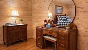 Ein Zimmer mit Holzwandverkleidung, einem Bett, einem Schminktisch, einem Spiegel und einem Nachttisch mit Lampen und einer Pflanze.