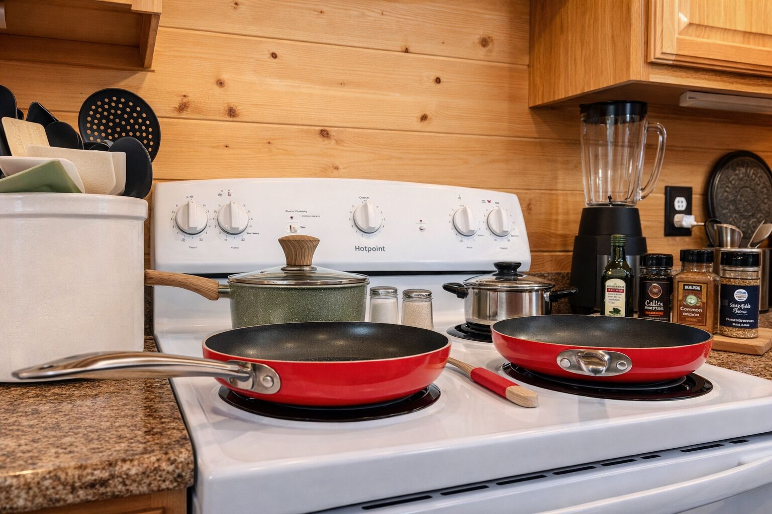 A kitchen with a white stove, two red frying pans, a pot, and various kitchen utensils.