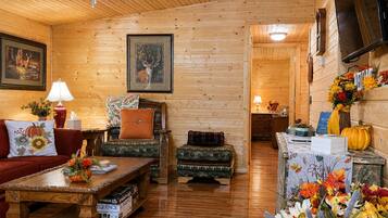 A cozy cabin interior with wooden walls, a sofa, a table with books, and a fireplace.