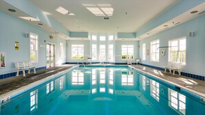 Ein großer, überdachter Swimmingpool mit klarem, blauem Wasser, umgeben von hellblauen Wänden und Fenstern.