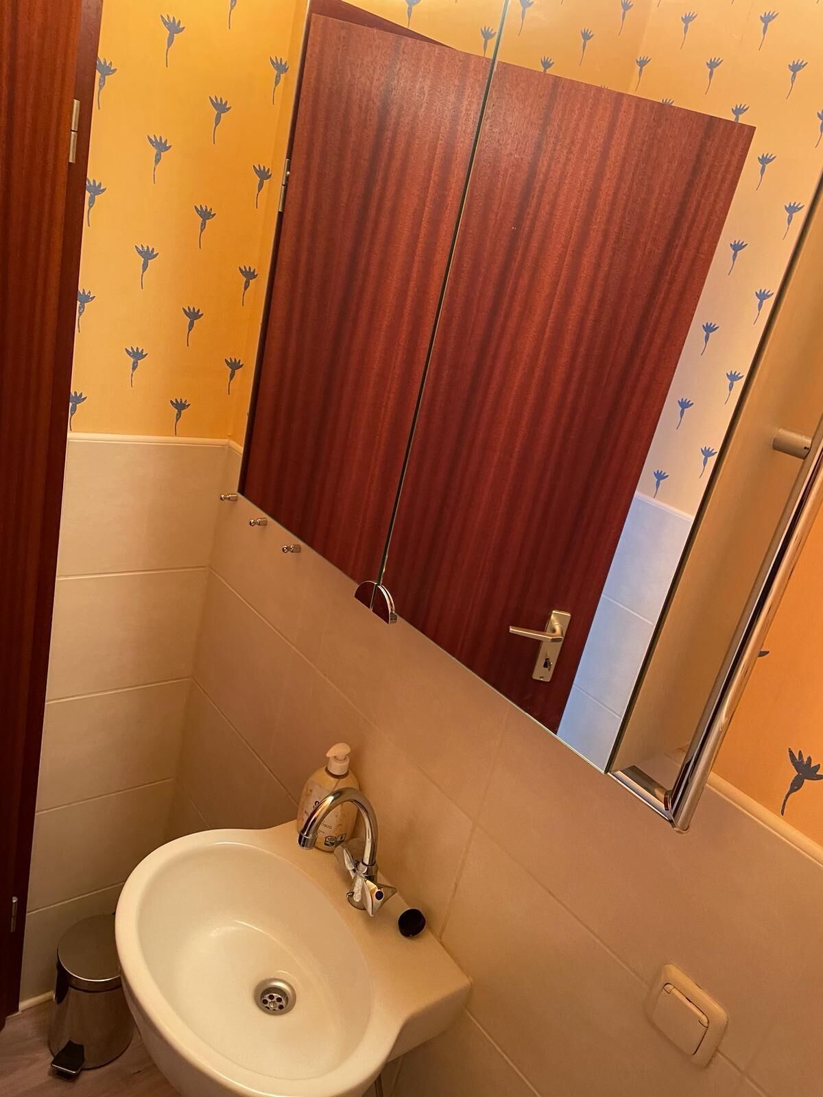 Een badkamer met een houten kastje, een wastafel en een spiegel.