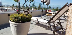A rooftop terrace with a large potted plant, a metal chair, and a table with chairs. - Beautiful Condo With Pool and Close to the Beach (Puerto Vallarta)
