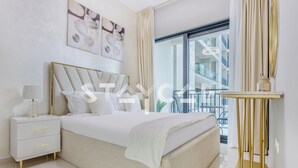 A modern bedroom with a bed, bedside tables, and a view of a balcony. - Staycae Holiday Homes - ZADA (Dubai)