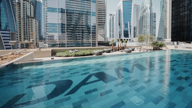A swimming pool with a geometric tile pattern, surrounded by modern high-rise buildings. - Staycae Holiday Homes - ZADA (Dubai)