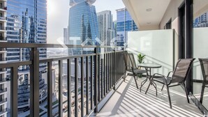 A balcony with a glass railing, two chairs, a small table, and a potted plant. - Staycae Holiday Homes - ZADA (Dubai)