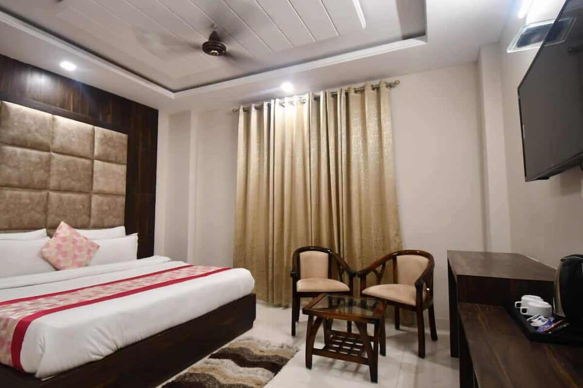 A hotel room with a large bed, two chairs, a small table, a TV, and curtains.