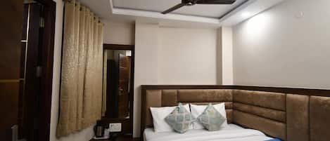 Un dormitorio con una cama, ventilador de techo, ventana con cortinas y mesita de noche con cafetera.