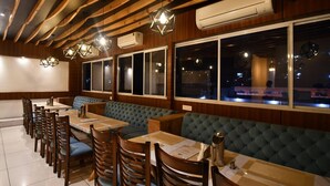 Un restaurante con vigas de madera en el techo, asientos tapizados en verde y varias mesas con sillas.