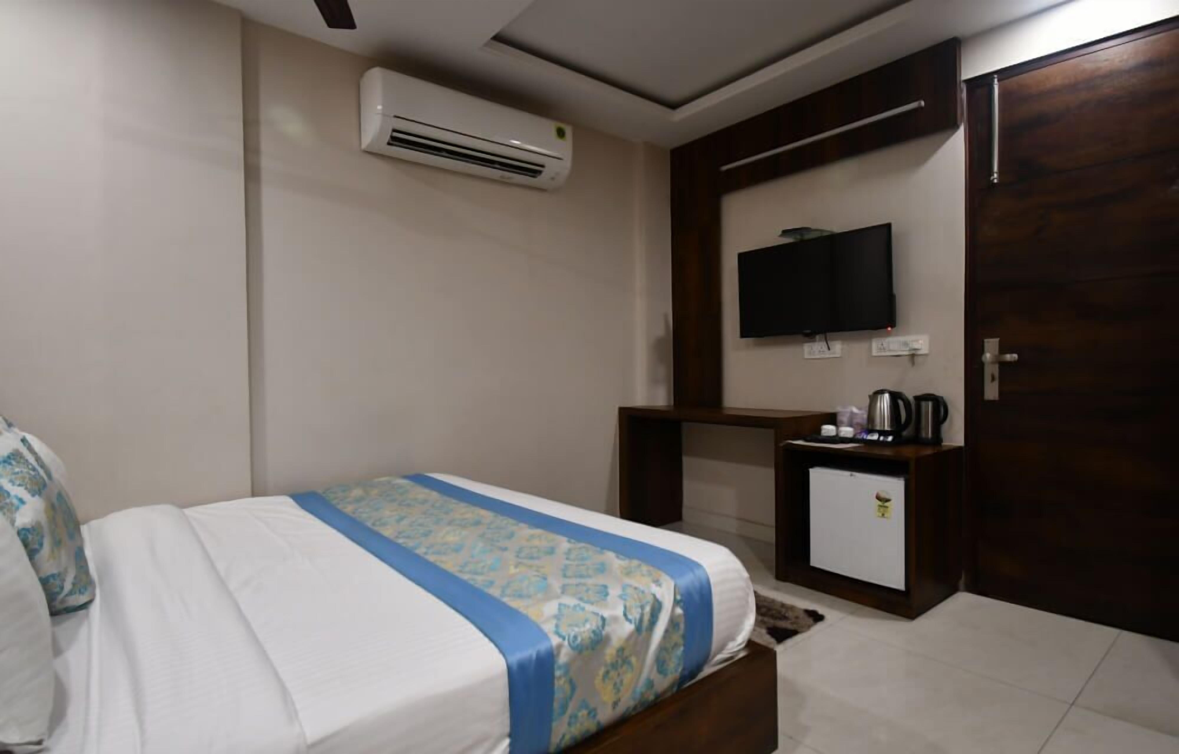 A hotel room with a bed, a desk, a television, and an air conditioning unit.