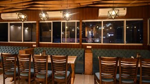 Un restaurante con paneles de techo de madera, asientos tapizados en tonos verdes y sillas de madera con cojines azules.