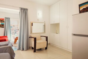 Relax in a comfortable seating area with a sofa and chair, featuring a cabinet and a large window with curtains.