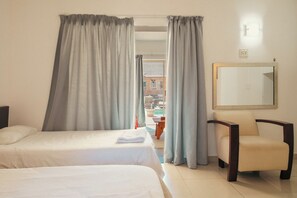 Two single beds with white linens, a nightstand, and armchair create a cozy space.