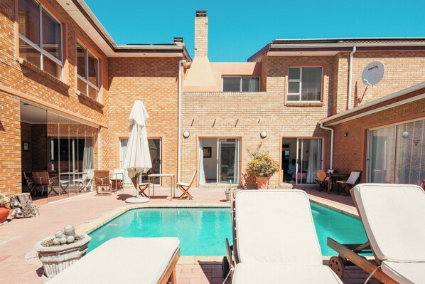 Relax by the pool surrounded by lounge chairs and a sun umbrella, with brick walls and large windows providing ample natural light.