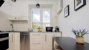 A modern kitchen with white cabinets, a dishwasher, a stove, and a window with a view of buildings. - Stylish Apartment with Balcony | Close to Zoo and Workspace (Warszawa)