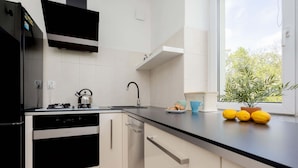 A modern kitchen with white cabinets, a black countertop, a built-in oven, and a window with a view of trees. - Stylish Apartment with Balcony | Close to Zoo and Workspace (Warszawa)