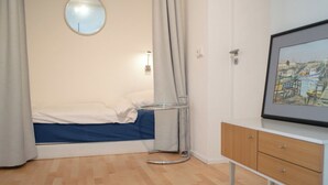 Un dormitorio con cama, mesita de noche, espejo, cuadro enmarcado y ventana con cortinas.