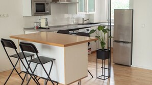 Una cocina moderna con una isla central, taburetes de bar, microondas, estufa y refrigerador.