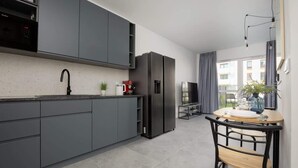 Une cuisine moderne avec des meubles gris, un réfrigérateur noir et un coin repas comprenant une table et des chaises.
