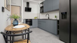 Une cuisine moderne avec des meubles gris, un réfrigérateur noir et une table à manger en bois, accompagnée de chaises.