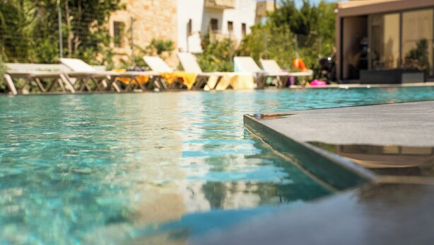 A swimming pool with lounge chairs and a stone building in the background. - La Rêve Luxury Apartments (Hersonissos)