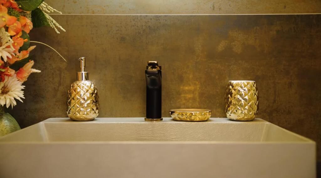 Ein Badezimmerwaschbecken mit zwei Seifenspendern mit goldener Musterung und einem schwarzen Wasserhahn.