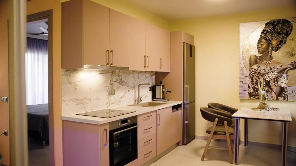 Una cocina moderna con armarios de colores claros, salpicadero de mármol, un refrigerador y un comedor con mesa y sillas.