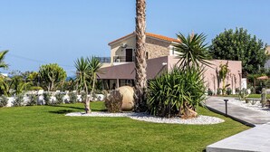 A house with a tall palm tree in the front yard, surrounded by various plants and a well-maintained lawn. - La Rêve Luxury Apartments (Hersonissos)