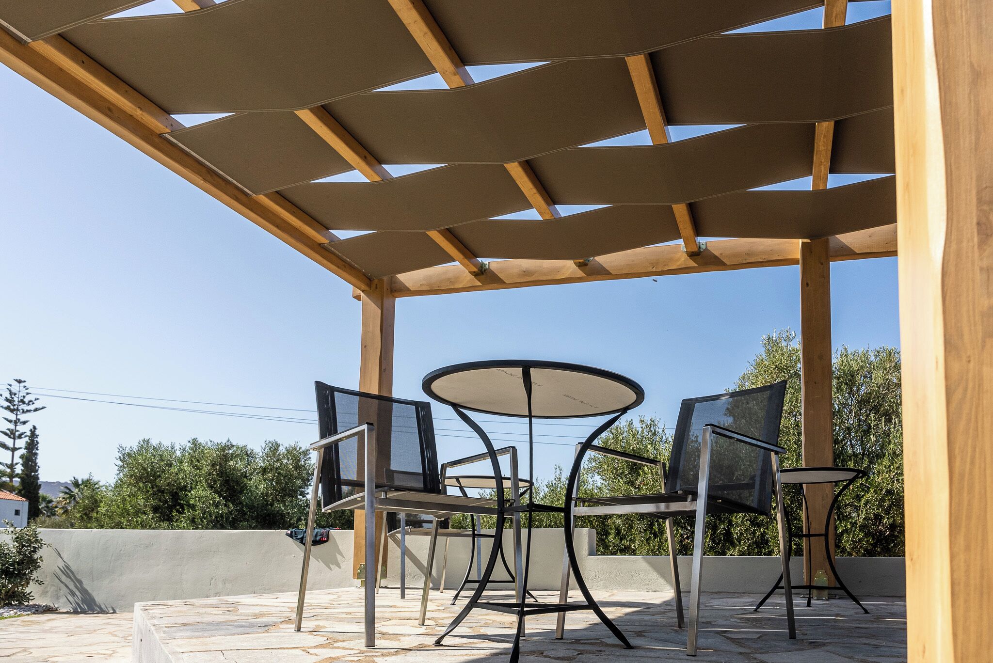 Un patio al aire libre con una pérgola, una mesa redonda y cuatro sillas.