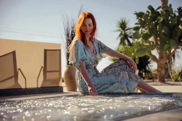 A person sitting on a hot tub with a clear sky and cacti in the background. - La Rêve Luxury Apartments (Hersonissos)