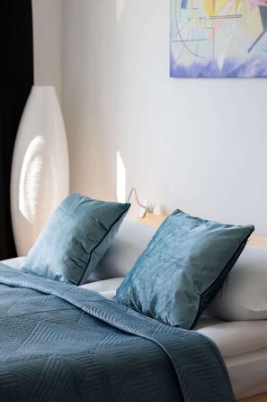 Een slaapkamer met een bed, twee kussens, een deken en een wandlamp.