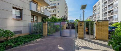 A gated entrance to a residential building with a paved walkway, a solar panel, and a sign indicating a 'Best Security' rating.