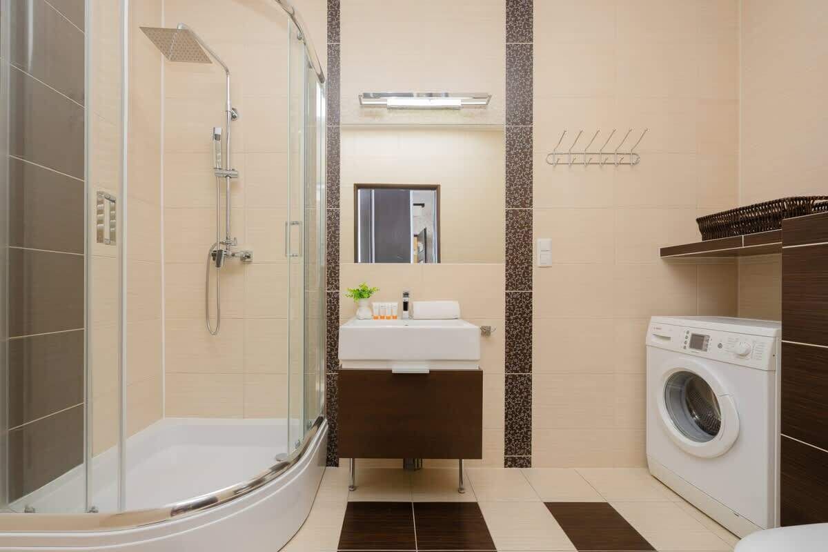 A modern bathroom with a glass-enclosed shower, a sink with a mirror, and a built-in washing machine.
