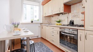A modern kitchen with light-colored cabinets, a gas stove, and a built-in oven. There is a window providing natural light and a small plant on the windowsill.