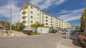 A multi-story residential building with balconies, a gated parking area, and a paved walkway.