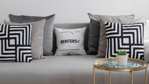 A sofa with patterned pillows, one with "RENTERS" text, and a small round table with a plant.