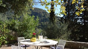 Eine Terrasse im Freien mit einem runden Tisch und vier Stühlen, umgeben von Pflanzen und einer Steinmauer.