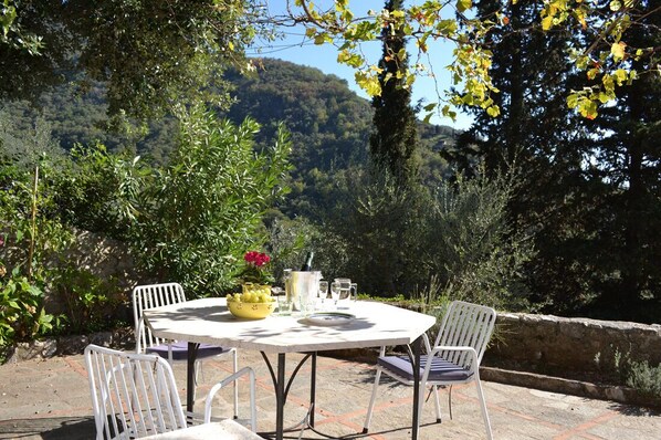Un patio al aire libre con una mesa redonda y cuatro sillas, rodeado de follaje y un muro de piedra.