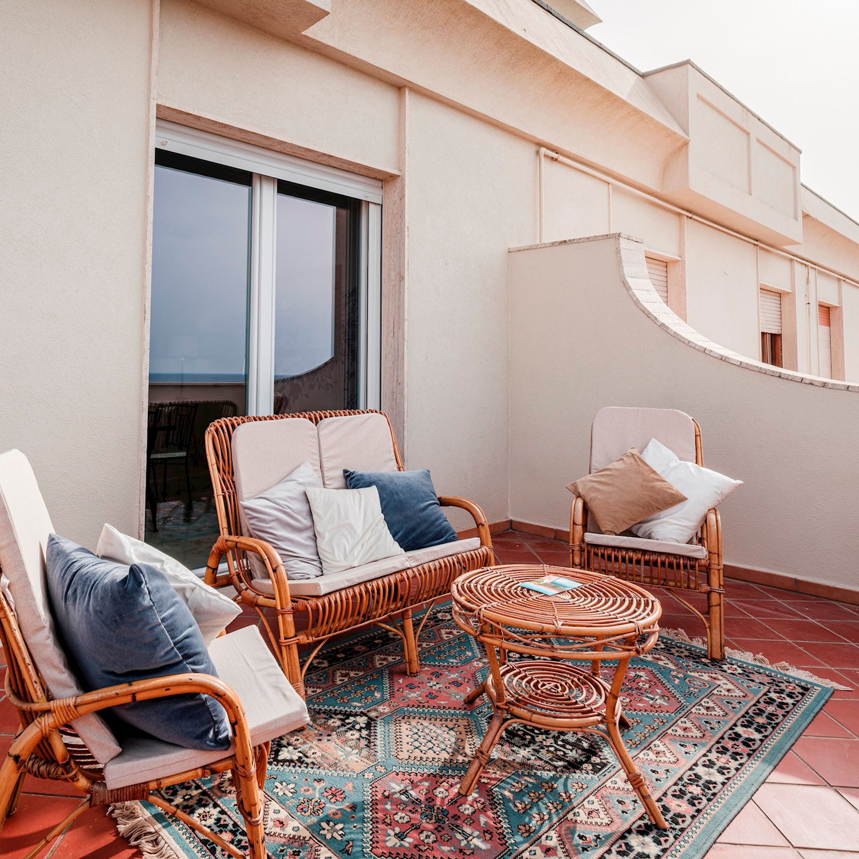 En balkon med fletningsmøbler, et mønstret tæppe og et stort vindue.