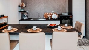 Una cocina moderna con una isla central, lámparas colgantes negras y un área de comedor con sillas color beige.