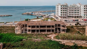Vista costera con un puerto deportivo, un edificio de varios pisos y una estructura en construcción.