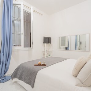 A bedroom with a bed, a TV, a shelf with items, and a window with curtains. - Luce Apartment in Como (Como)