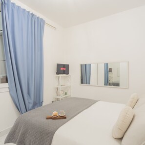 A hotel room with a bed, a TV, a mirror, and a shelf with a tray of food. - Luce Apartment in Como (Como)